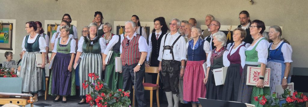 Der Singkreis Raaba in Tracht auf der Bühne am Stranzhof, mit roten Blumen im Vordergrund.