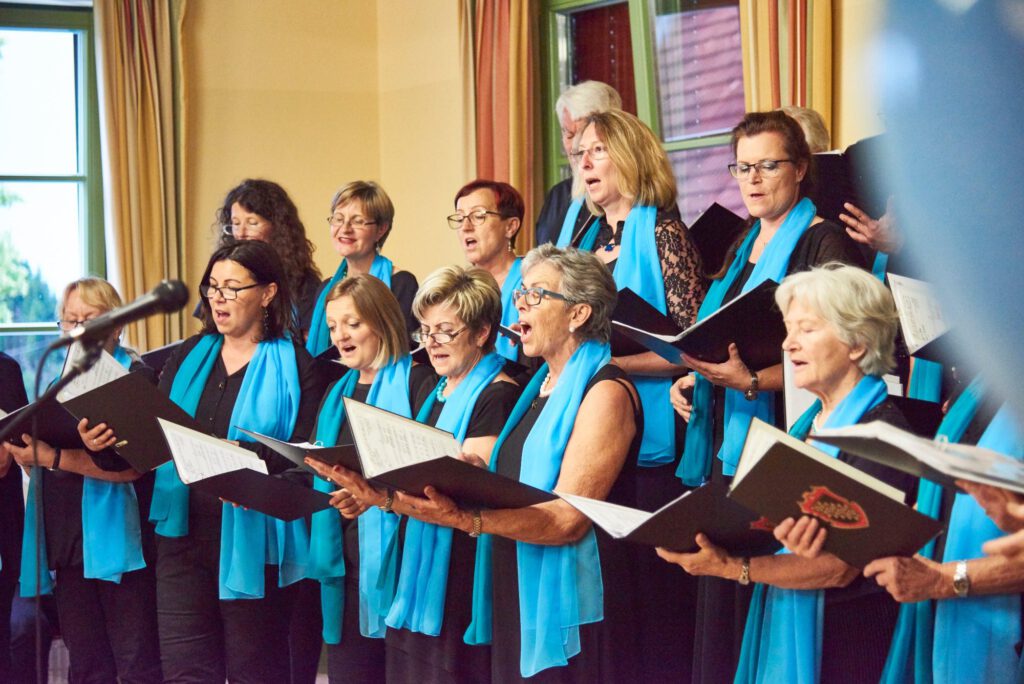 Sängerinnen des Singkreis Raaba in Schwarz mit hellblauen Schals singen aus ihren Notenmappen