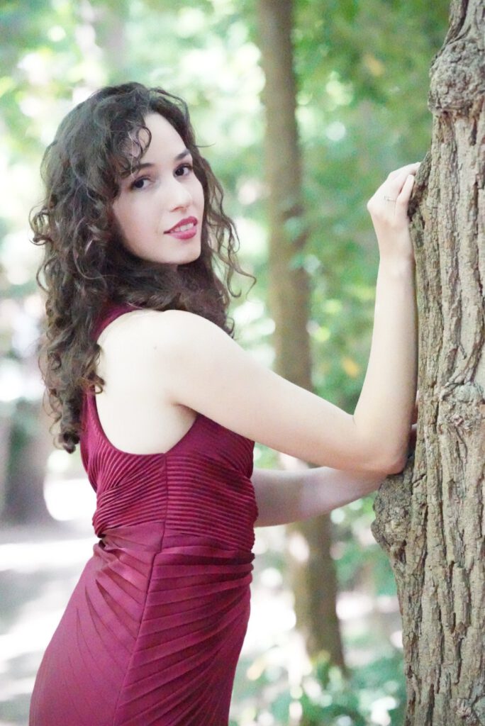 Porträt Teodora Ateljević in einem dunkelroten Kleid an einem Baumstamm